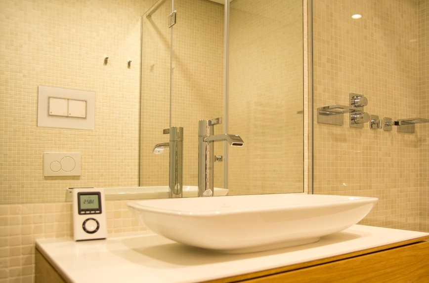 Modern bathroom in an apartment in Budva, Montenegro: countertop sink, glass shower, and beige tiles.
