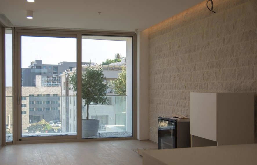 Living room with panoramic windows and a stone wall in a new apartment in Budva, Montenegro. View of the city and the terrace.