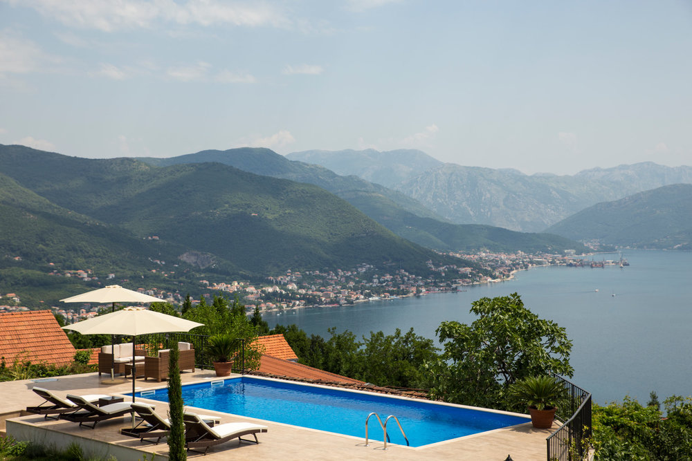 Open-air swimming pool at a villa in Luštica, Montenegro, with panoramic views of the Bay of Kotor and the mountains, sun loungers and a terrace.