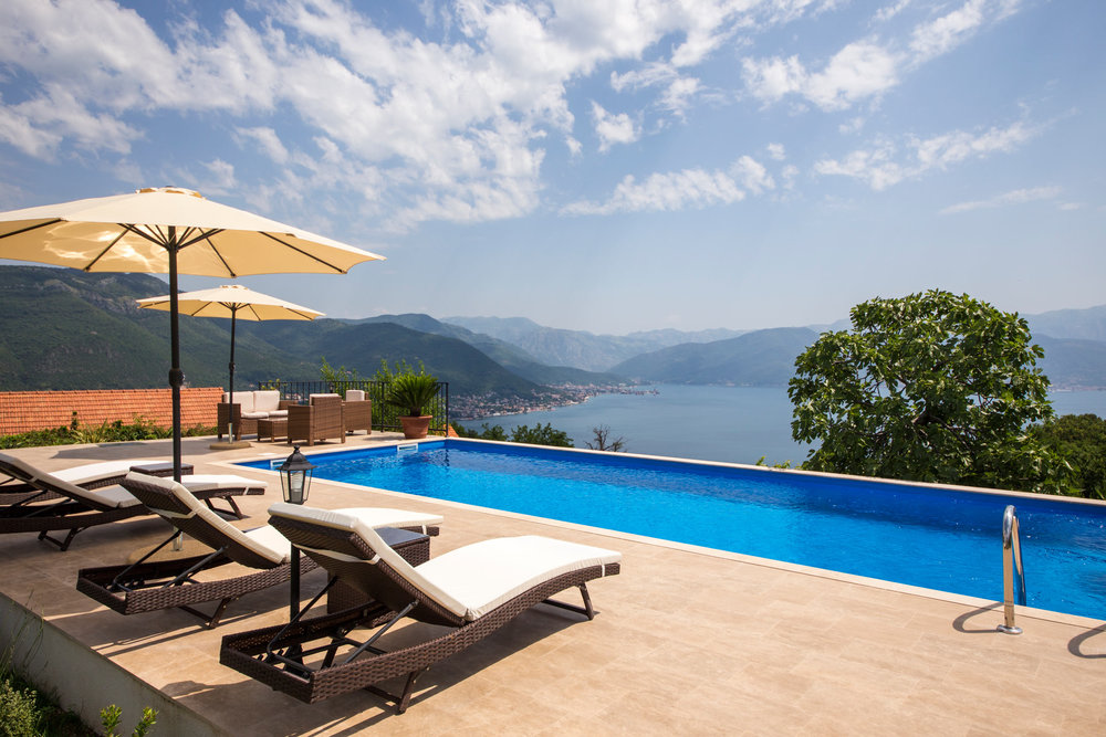 Swimming pool with panoramic views of the Bay of Kotor and the mountains at a villa in Luštica, Montenegro, with sun loungers and umbrellas.