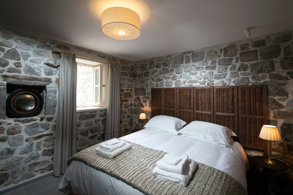 Bedroom with stone walls and a woven headboard on a villa in Luštica, Montenegro.
