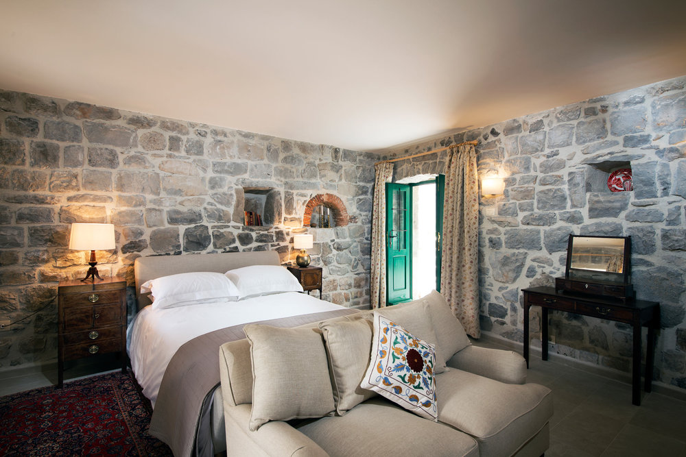 Bedroom in a villa in Luštica, Montenegro: stone walls, a double bed, a sofa, and antique furniture in the interior.
