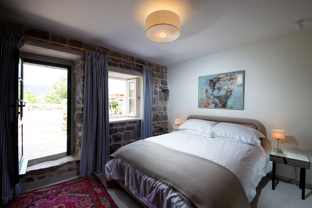 Bedroom in a villa in Luštica, Montenegro: stone walls, a double bed, access to the terrace, and a vintage rug.