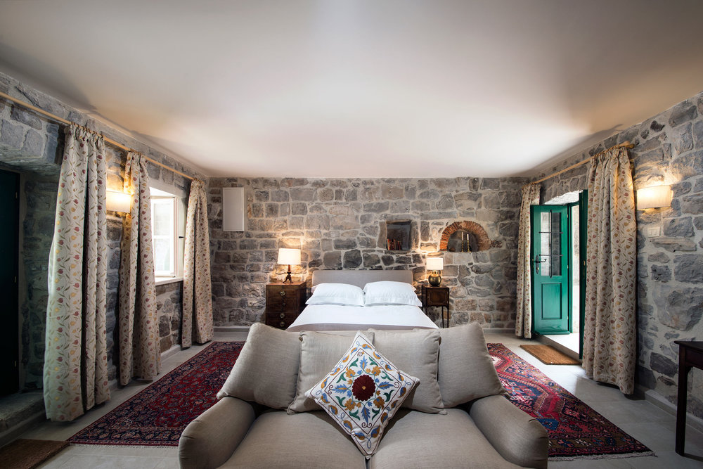 Bedroom in a stone villa on the Luštica Peninsula, Montenegro: bed, vintage furniture, and authentic stone masonry.
