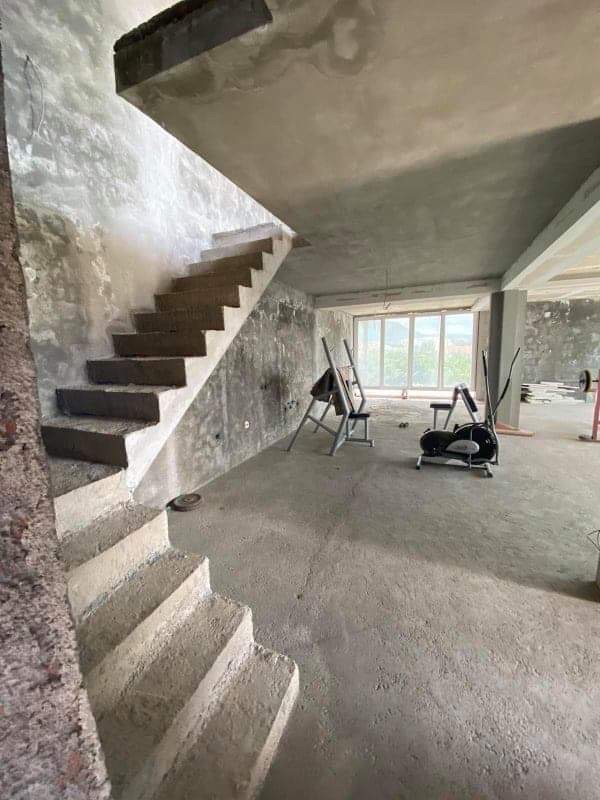 Two-level house in Shushan, Montenegro: concrete staircase, rough finish, and exercise equipment in a spacious room.