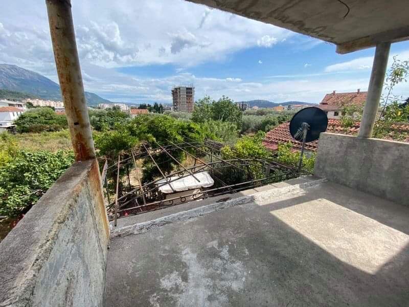 Open terrace of a house in Shushan, Montenegro, with a view of the mountains, a green garden, and urban development, ready for finishing.