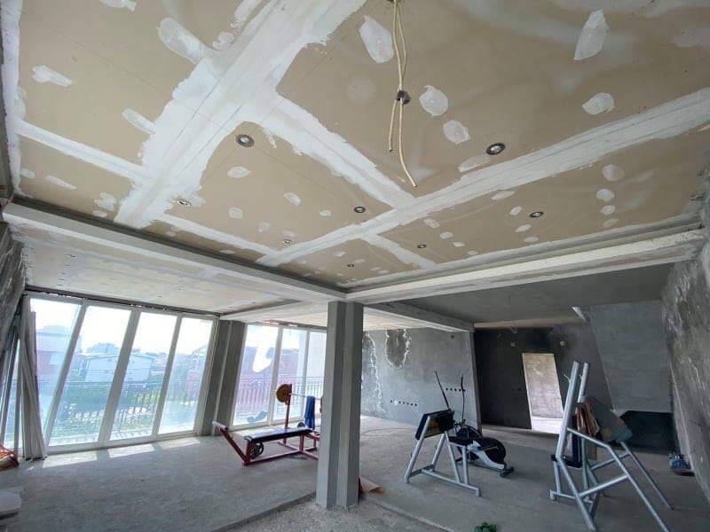 Living room under renovation in a house in Shushan, Montenegro: panoramic windows, drywall ceiling, and exercise equipment.