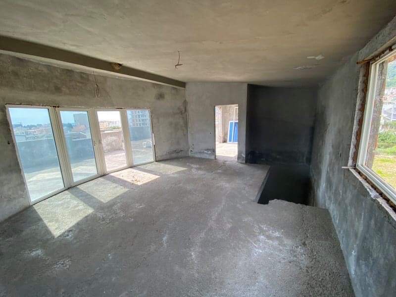 Living room unfinished in a house under construction in Shushan, Montenegro: concrete walls, panoramic windows, and access to the terrace.