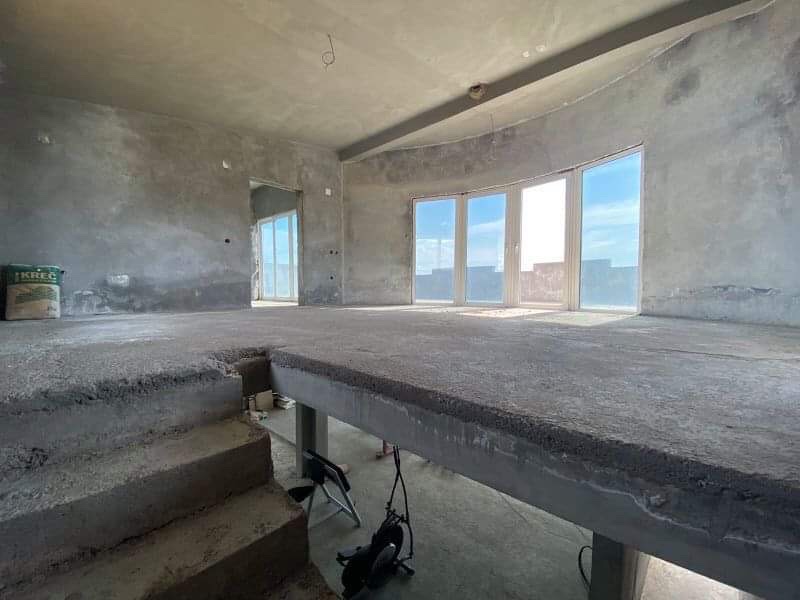 Living room in a house ready for finishing in Šušanj, Montenegro: concrete floors, panoramic windows, and sea view.