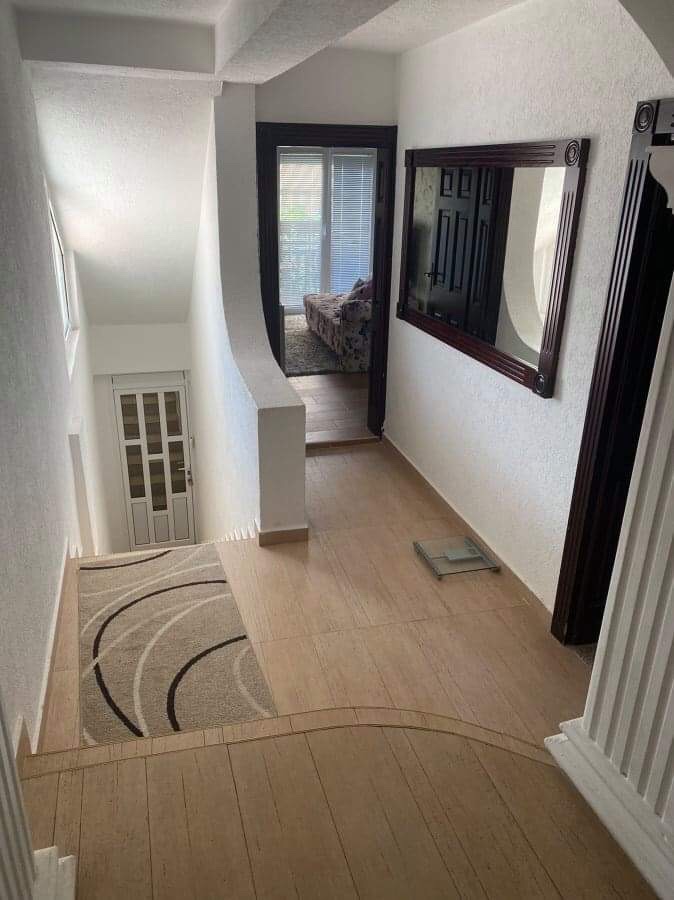 Bright hallway with a staircase and mirror in a house, Shushan, Montenegro. Tiled floor, white walls, and a view into the room.
