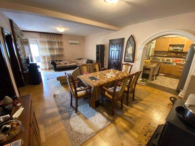 Living room with dining area in a house in Shushan, Montenegro: parquet flooring, wooden furniture, and an arched passage to the kitchen.