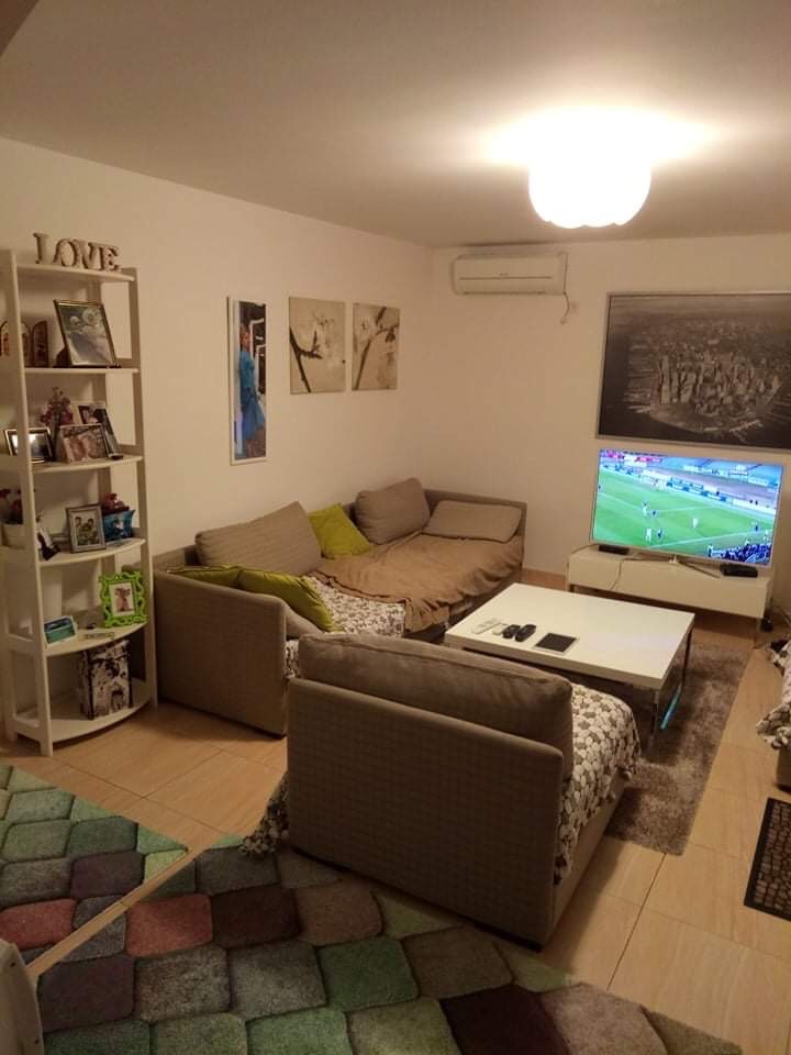 Cozy living room with a sofa and TV in a house in Šušanj, Montenegro: bright interior, shelving unit, and air conditioner.