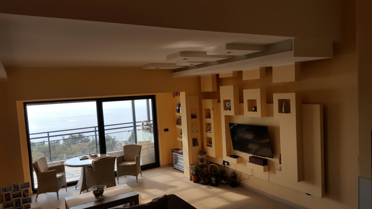 Living room in a house in Shushan, Montenegro: designer TV wall, panoramic windows, and a terrace with sea view.