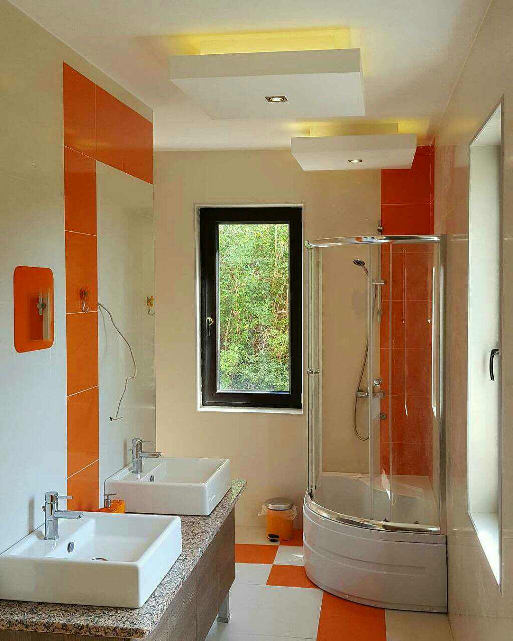 Bathroom in a house in Shushan, Montenegro: shower cabin, two sinks, orange tiles, and a window overlooking the garden.