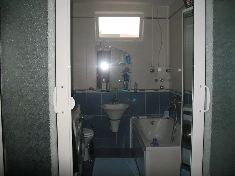 Bathroom with blue tiles, sink, bathtub, and toilet visible through an open white door frame.