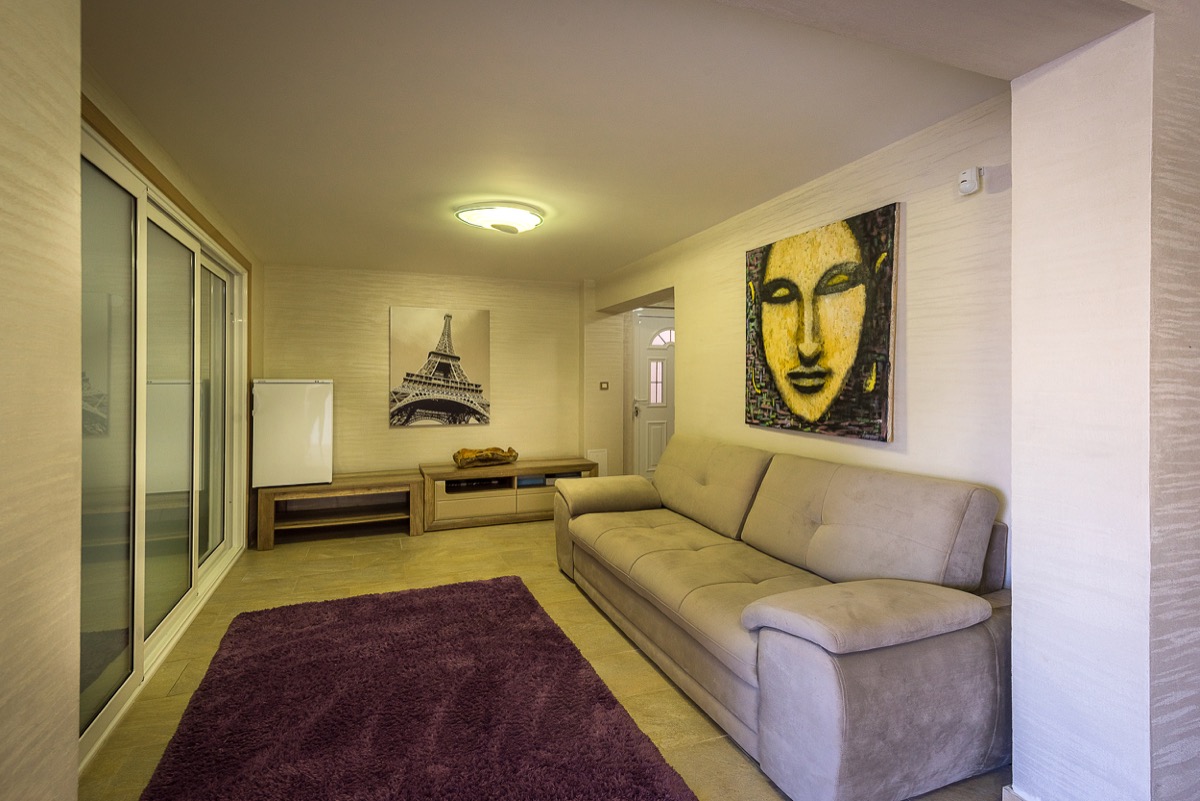 Living room in a villa in Krašići, Montenegro: beige sofa, purple rug, wall art, and panoramic windows.