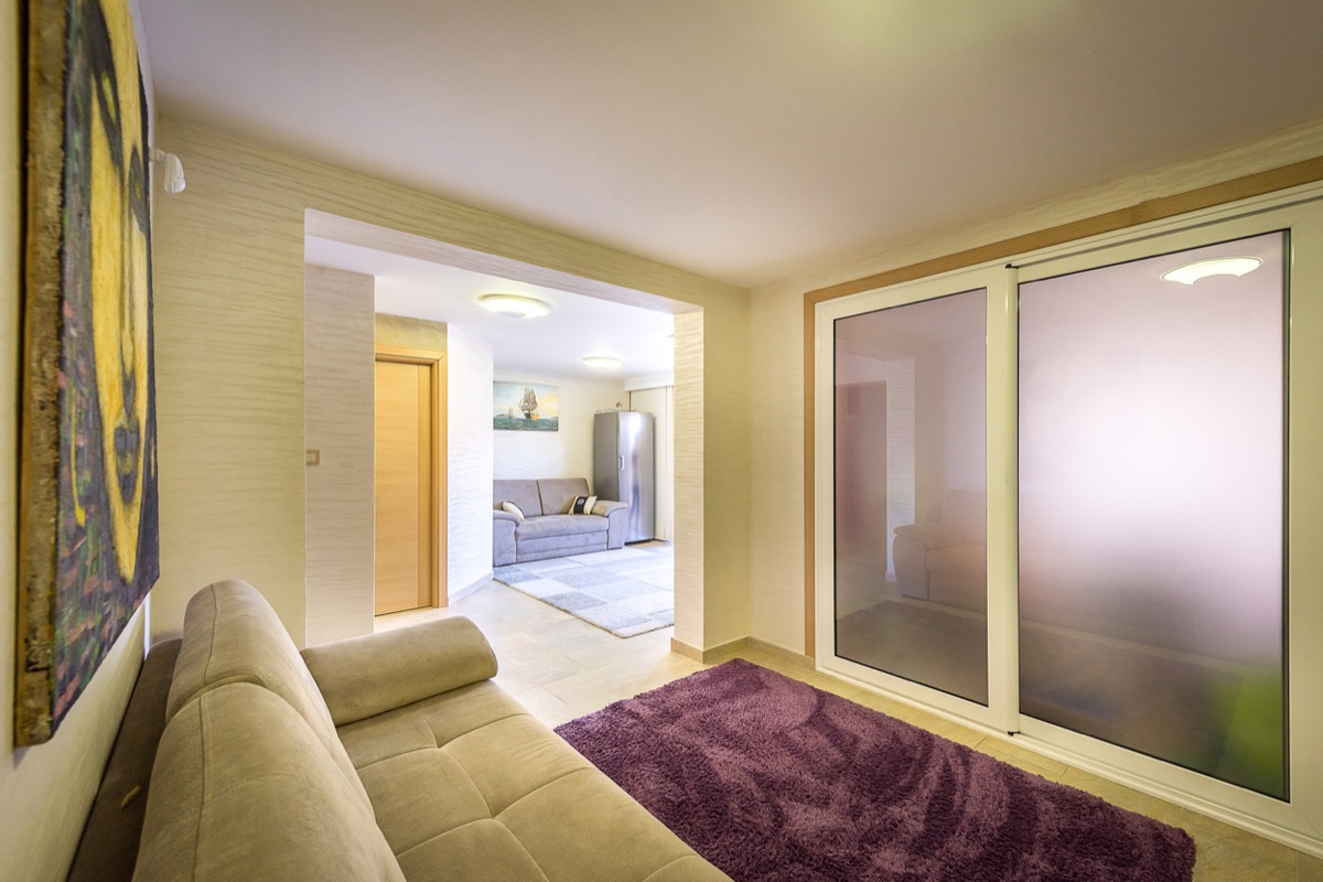 Living room interior in a villa in Krašići, Montenegro: light-colored furniture, panoramic windows, and a cozy purple rug.