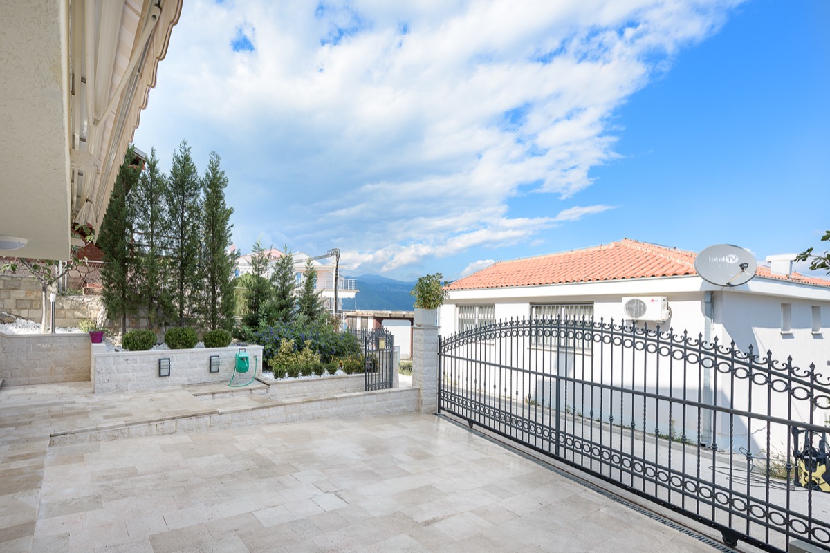Terrace and villa entrance in Krašići, Montenegro: stone finishes, wrought-iron gates, landscaping, and mountain views.