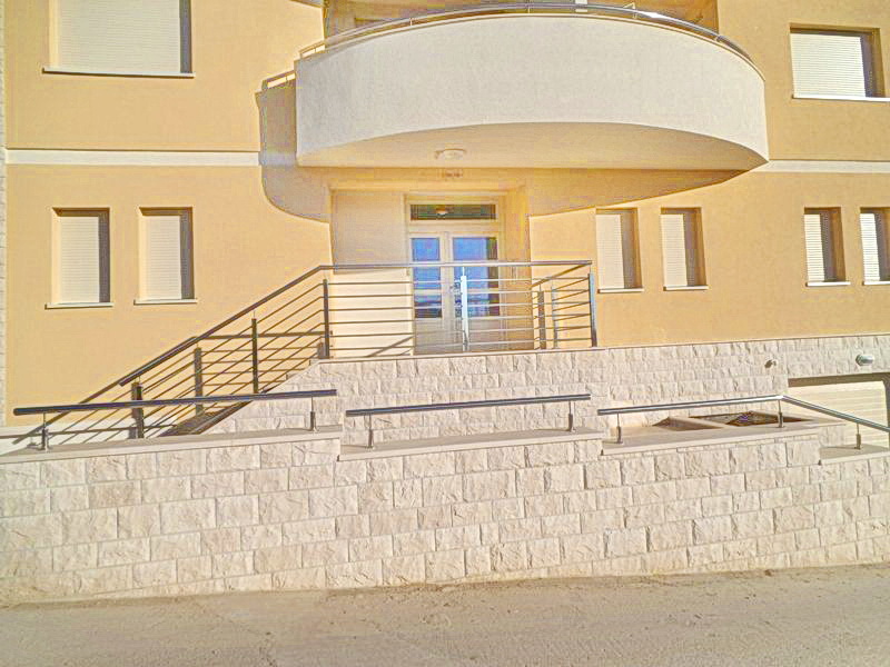 Hotel facade in Bečići, Montenegro: entrance area with stone cladding, metal railings, and a balcony.