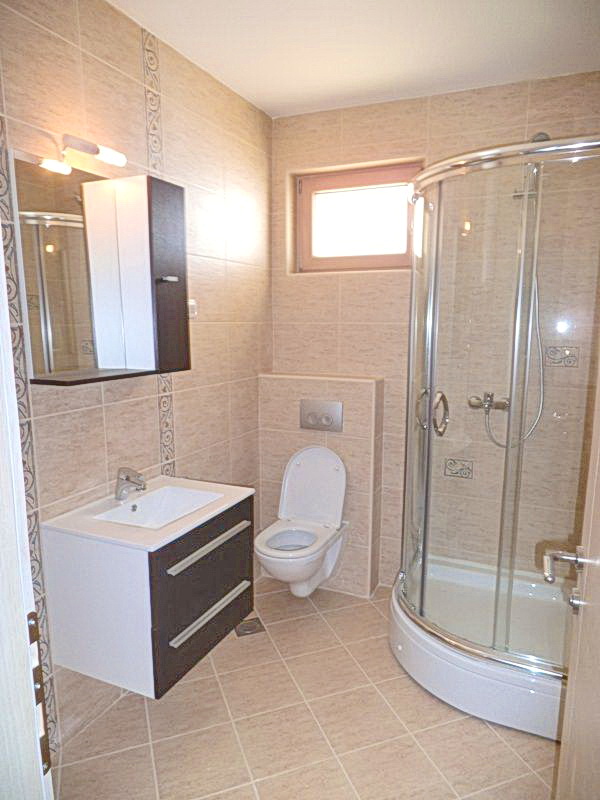 Modern bathroom with a shower cabin in a hotel in Bečići, Montenegro: light tiles, wall-mounted toilet, and vanity unit.
