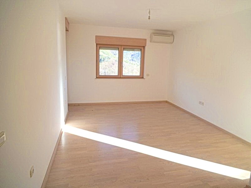 Bright empty living room in a hotel in Bečići, Montenegro: laminate flooring, white walls, air conditioning, and a mountain view from the window.