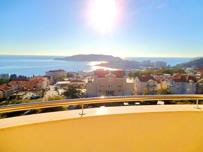 Panoramic view of the sea and island from the hotel balcony in Bečići, Montenegro, with a metal railing and bright sunlight.