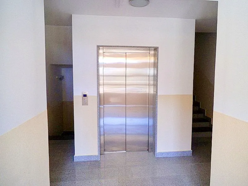 Elevator in a building hallway with stairs visible on the right and two-tone walls.