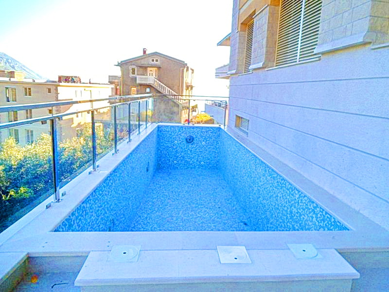 An outdoor swimming pool with mosaic finishing on the hotel terrace in Bečići, Montenegro, overlooking the city and mountains.