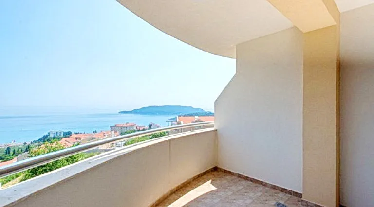 Empty curved balcony with a railing overlooking the sea and town.