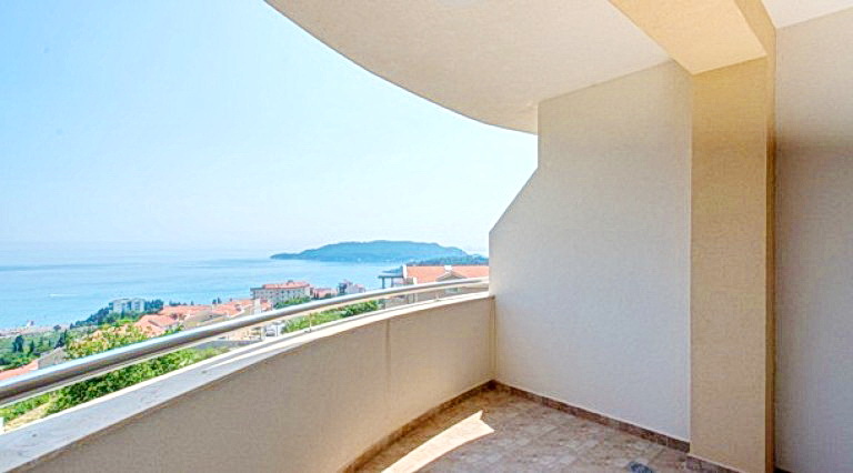 Spacious balcony with panoramic views of the sea and mountains at a hotel in Bečići, Montenegro, with tiled flooring and a railing.