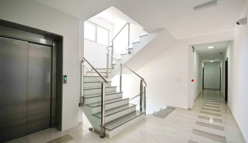 Modern entrance hall with elevator and staircase in a residential complex in Budva, Montenegro: bright interior, tile flooring, railings.