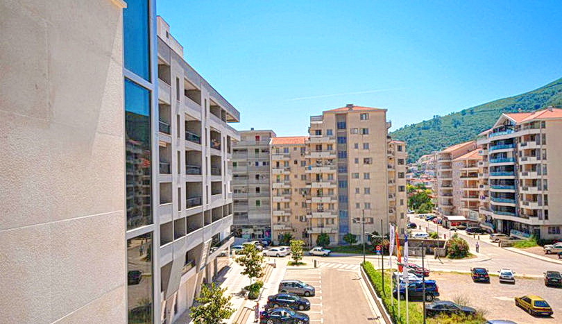 View of modern residential complexes and parking in the city of Budva, Montenegro, surrounded by mountains on a sunny day.