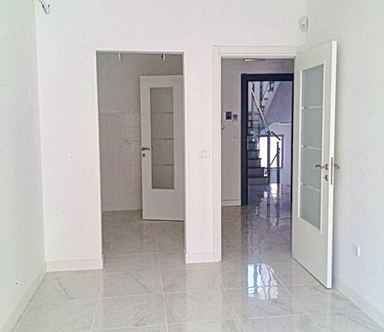 Bright living room with white finishes and glossy tiled flooring in a residential complex in Budva, Montenegro, view of the staircase.