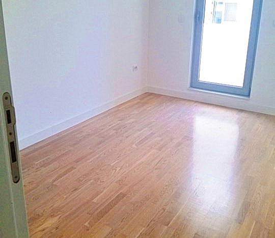 Bright empty bedroom with parquet flooring and access to the balcony in a residential complex in Budva, Montenegro.
