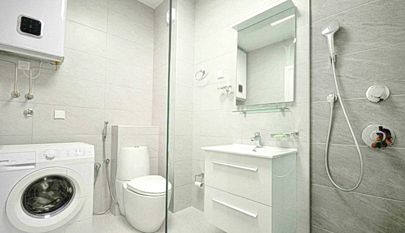 Modern bathroom with a shower cabin and washing machine in a residential complex in Budva, Montenegro. Light-colored tiles and sanitary ware.
