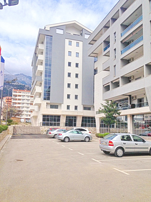 Modern residential complex with parking in Budva, Montenegro: building facade, panoramic windows, and mountain view.