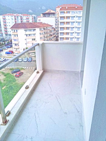 Bright balcony with tiled floor and glass railing in a residential complex in Budva, Montenegro, city view.