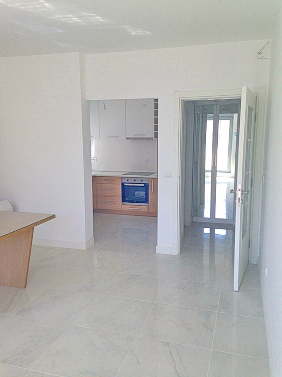 Living room with kitchen in a modern residential complex in Budva, Montenegro: light finishes, tiled floor, and built-in appliances.