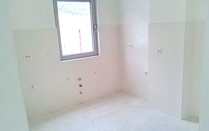 Room with white wall and floor tiles, a window, visible water supply pipes near the floor, and electrical outlets.