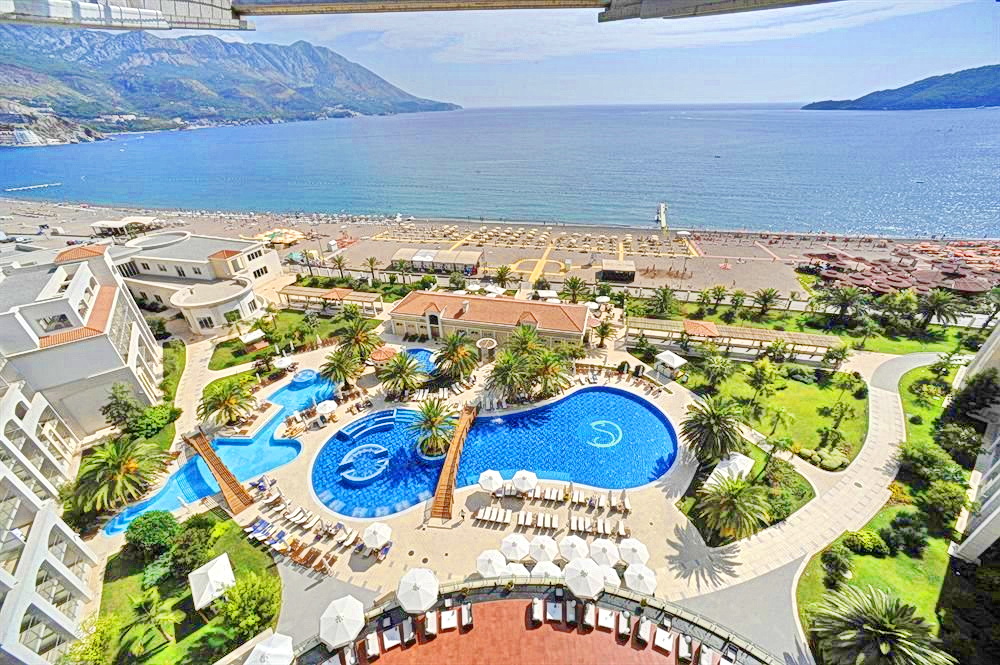 View from the balcony of the sea, beach, and hotel pool in Bečići, Montenegro: a panorama of the resort complex with palm trees.