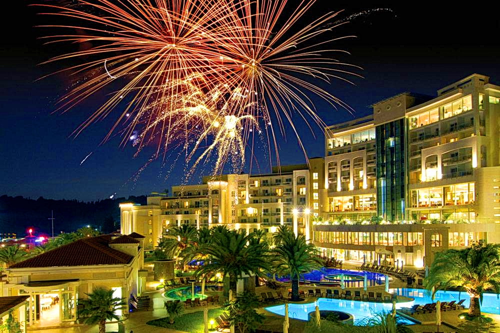 Night view of a luxury residential complex with a swimming pool and festive fireworks in Bečići, Montenegro.