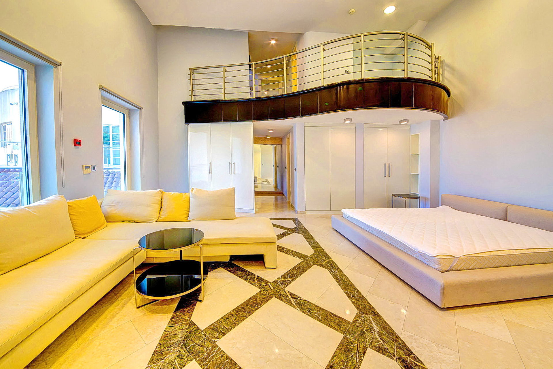 Two-level living room in an apartment in Bečići, Montenegro: light-colored furniture, marble floor, and a mezzanine balcony.