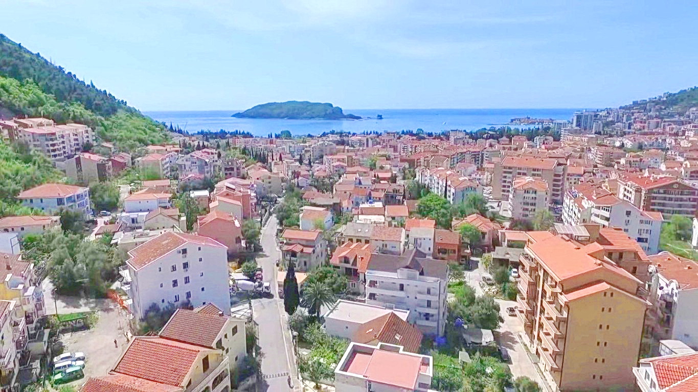 Panoramic view of the city of Budva in Montenegro, residential buildings with red roofs, mountains and the island of St. Nicholas on the horizon