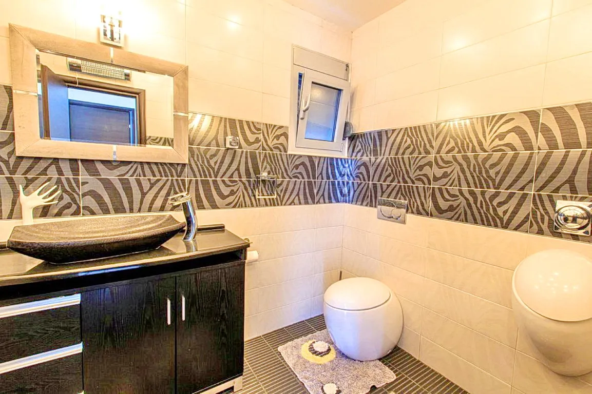 Bathroom with black vessel sink on vanity, toilet, and zebra-pattern wall tiles.