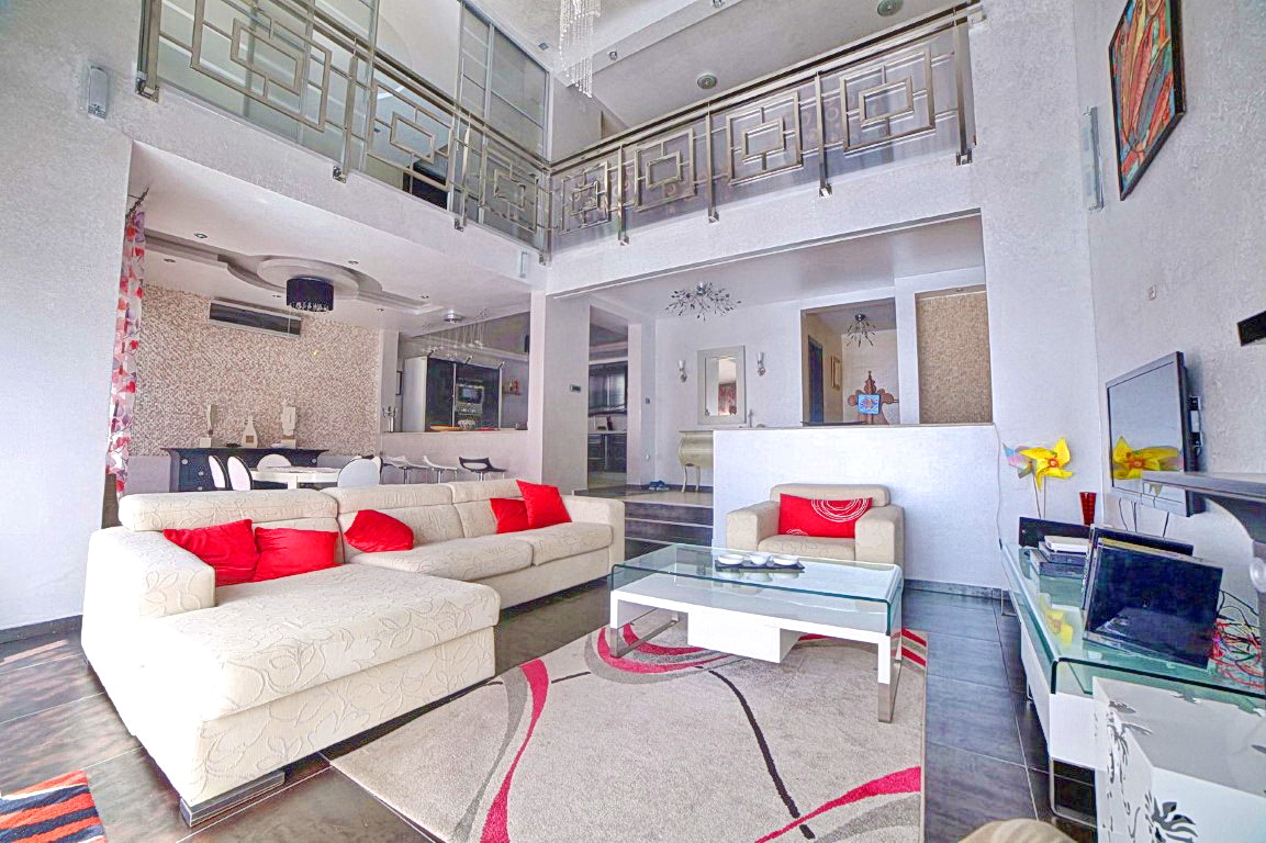 Spacious living room with double-height ceilings in a villa in Budva, Montenegro: a light-colored sofa, glass table, and modern decor.