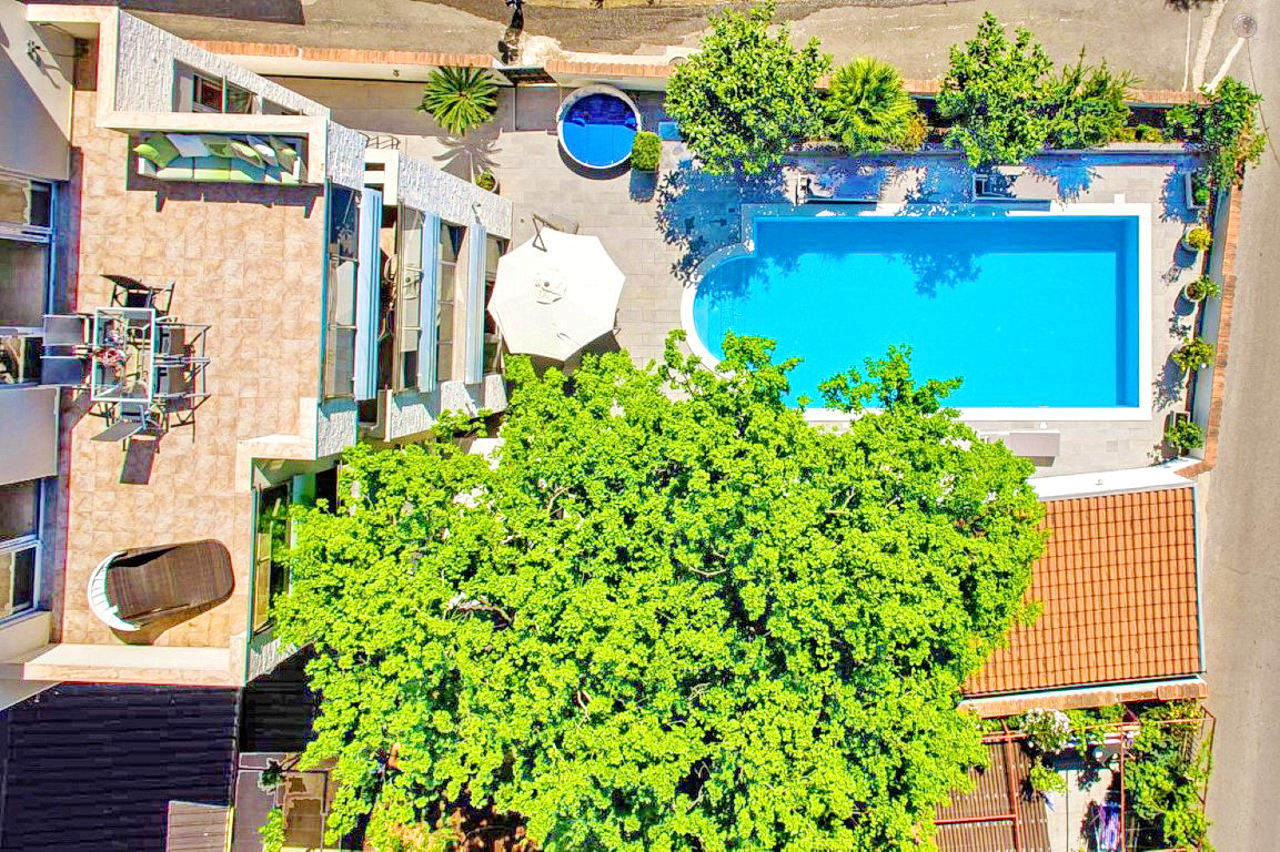 Top view of a villa in Budva, Montenegro: an open terrace with furniture, a swimming pool, a jacuzzi, and a garden with a large tree.