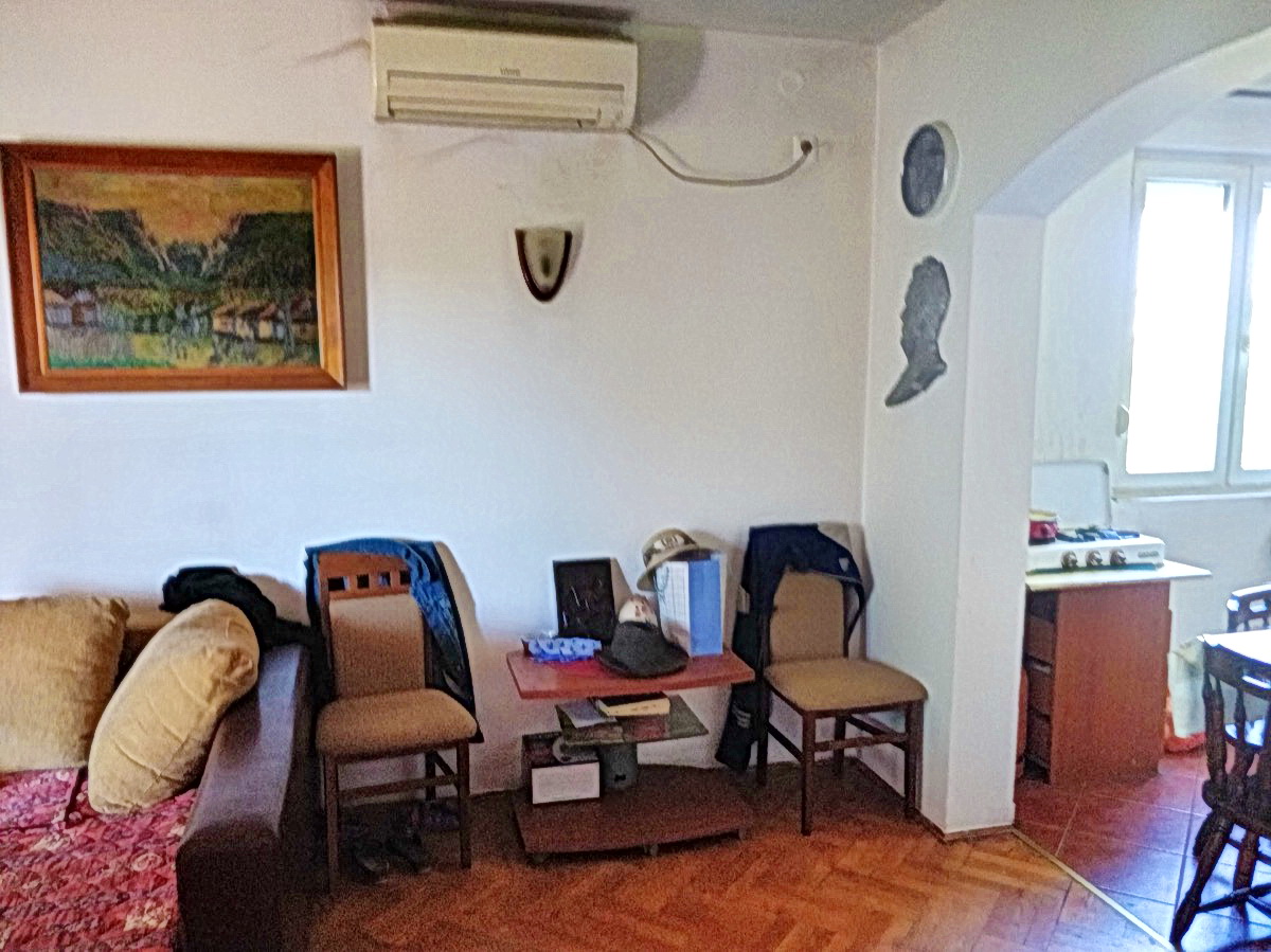 Living room in a house in Podgorica, Montenegro: a soft sofa, chairs, air conditioner, and passage to the kitchen with a stove.