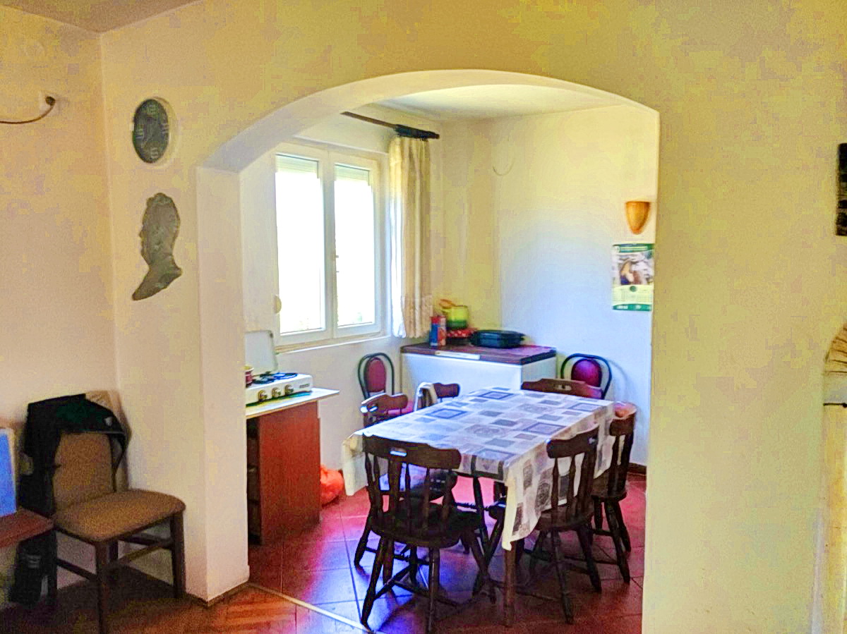 Kitchen-dining room in a house in Podgorica, Montenegro: dining table, wooden chairs, arched opening, and tiled floor.