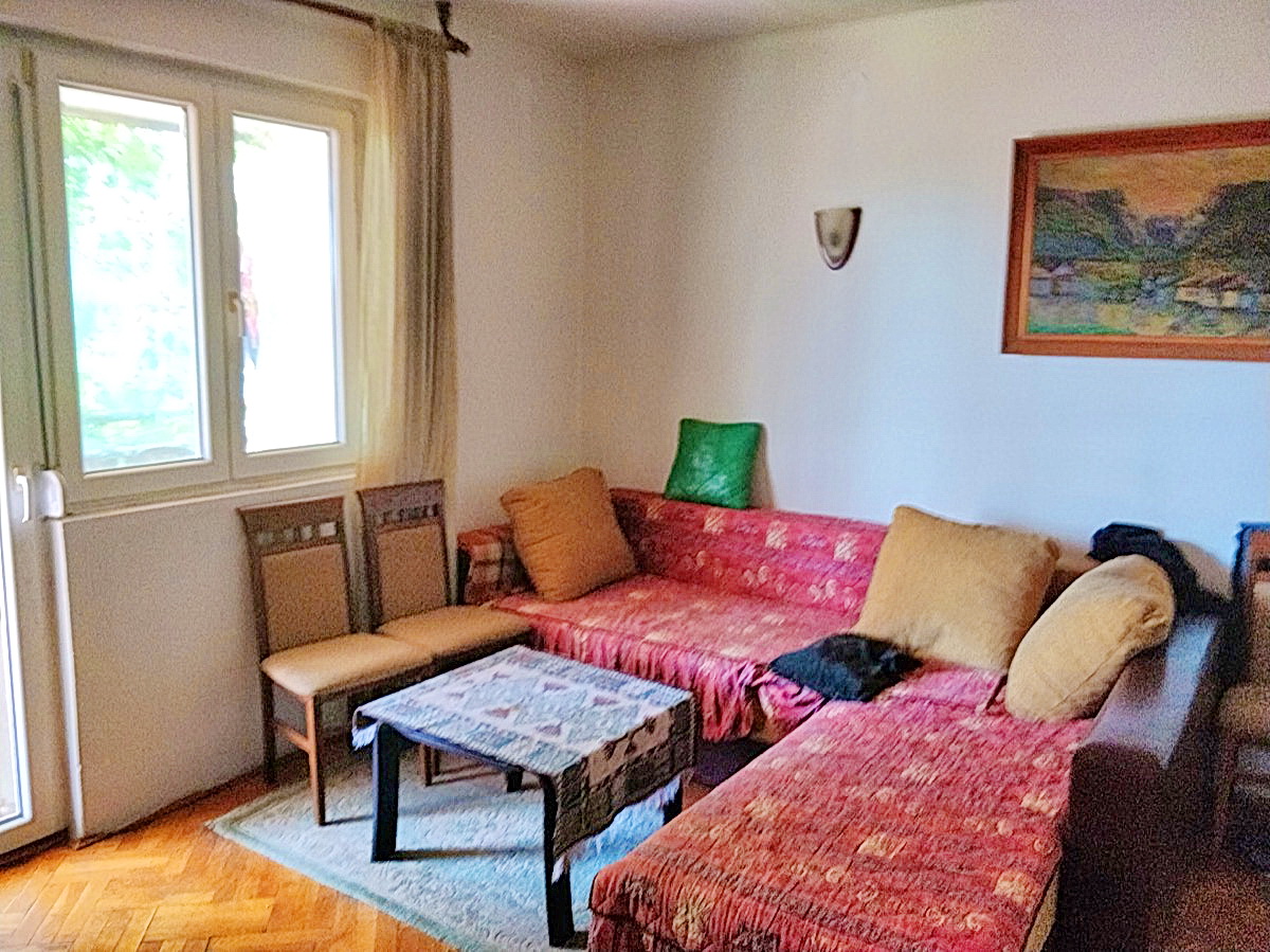 Living room in a house in Podgorica, Montenegro: red corner sofa, coffee table, parquet flooring, and light-colored walls.