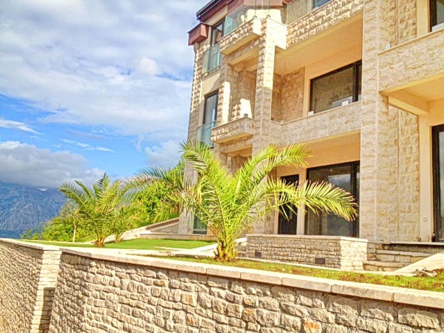 Facade of a residential complex made of natural stone with terraces and palm trees in Morinj, Montenegro.